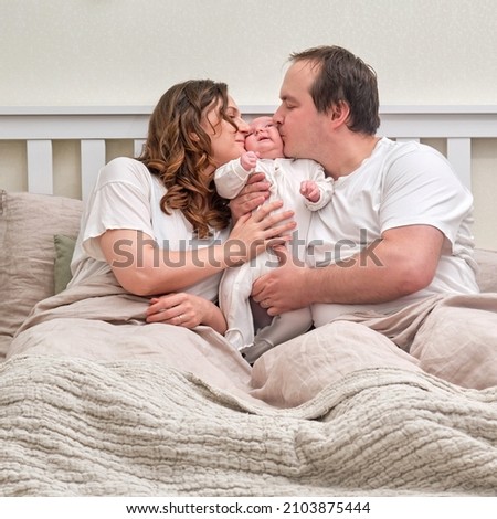 A man and a woman kiss a newborn baby on the bed. Father and mother of a child boy, happy parents and an infant baby in a home bedroom
