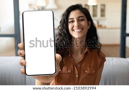 Mobile Advertisement. Happy Beautiful Woman Showing Big Blank Smartphone At Camera While Sitting On Couch At Home, Young Female Demonstrating Phone With White Screen For App Design, Collage, Mockup