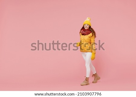 Full size body length exultant cheerful young woman 20s years old wears yellow jacket hat mittens looking camera walking stepping pacing isolated on plain pastel light pink background studio portrait Royalty-Free Stock Photo #2103907796