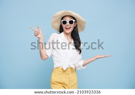 Young elegant beautiful Asian woman dressed in summer clothes smiling and pointing to empty copy space isolated on blue background. Royalty-Free Stock Photo #2103923336