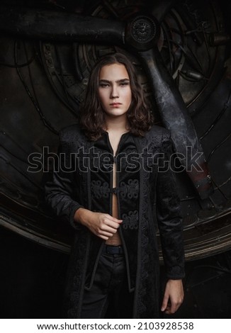 Dark hair handsome young boy in wearing in black shirt and black jeans sits and posing on the background of an old and rusty turbine aircraft 