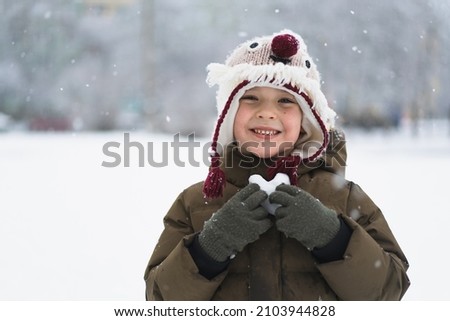 Child enjoying winter. The boy holds a heart made of snow in his hands in winter day. Love concept. Outdoors winter activities for kids. Winter Christmas and lifestyle concept.