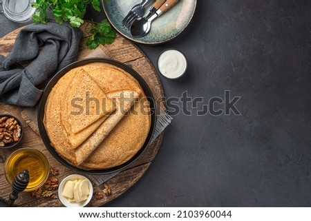 Stack pancakes on a dark background with honey, sour cream and nuts. Russian blini. Mardi Gras. Top view, copy space.
