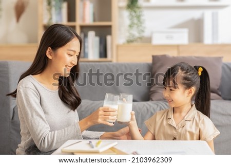 Asian mother and her daughter clink glasses enjoy and smile with milk drink.Mom and little girl holding milk glasses and drink to get calcium.Healthy Eating Concept Royalty-Free Stock Photo #2103962309