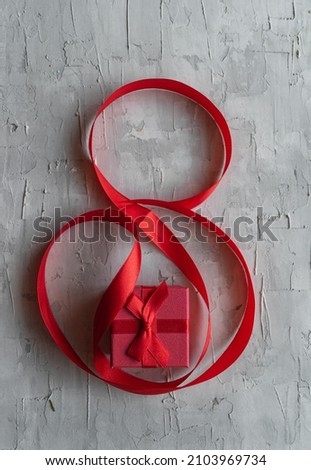 On a gray background, a red ribbon in the form of an eight with a gift. A holiday card. March eighth. Women's Day.