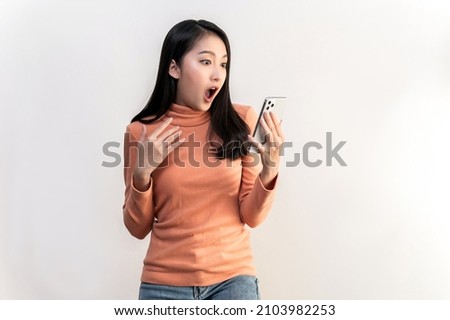 Portrait photo of young beautiful Asian woman feeling happy or surprise shock and looking at smart phone on white background can use for advertising or product presenting concept. Royalty-Free Stock Photo #2103982253