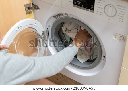 Woman's arm filling the washing machine drum. Concept of energy consumption, high price of electricity, household chores, housewives, turning on the washing machine.