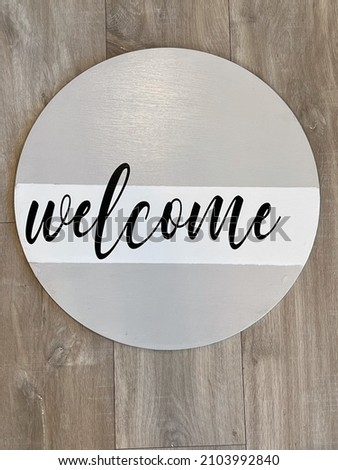 Homemade DIY craft round wood welcome sign with gray and white background and black cursive font reading "welcome."