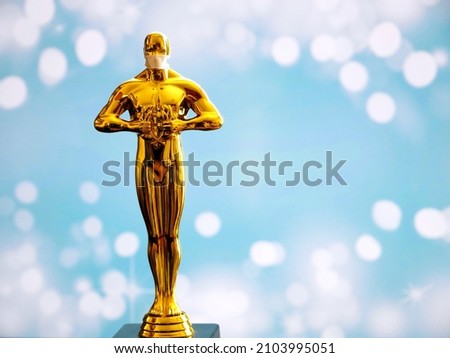Hollywood Golden Oscar Academy award statue in medical mask on blue background. Success and victory concept. Oscar ceremony in coronavirus covid-19 time
