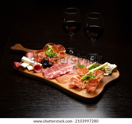 Two red wine glasses with buffet platter with cheese and meats, antipasti, prosciutto, charcuterie. Royalty-Free Stock Photo #2103997280