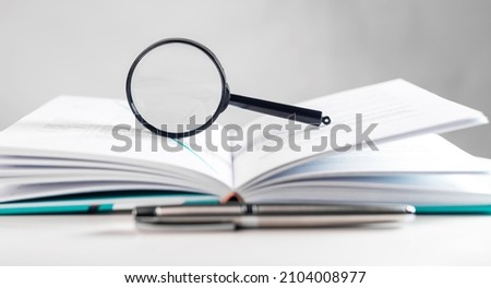 Magnifying lens over open paper book with pages. Concept of academic research. Royalty-Free Stock Photo #2104008977