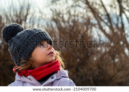 Caucasian blonde toddler girl with wool cap and red scarf on one side of picture, looking up