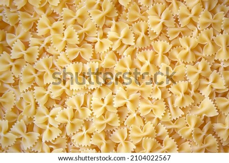 A lot of pasta in the shape of a butterfly on the table as a background, texture. Royalty-Free Stock Photo #2104022567