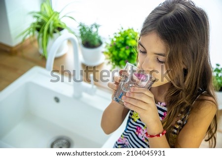 Children picks up a glass of water from the tap. Selective focus. Kid.