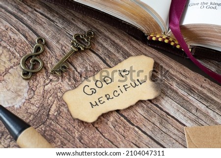 God is Merciful, handwritten Bible quote with an old, vintage key and treble clef on a wooden table. Christian biblical concept of Jesus Christ's grace and love. A closeup. Royalty-Free Stock Photo #2104047311