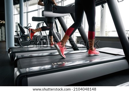 Female and male legs in trainers running on treadmills in gym. Active unrecognisable couple exercising to stay fit and healthy. Togetherness and support in sport concept. Royalty-Free Stock Photo #2104048148