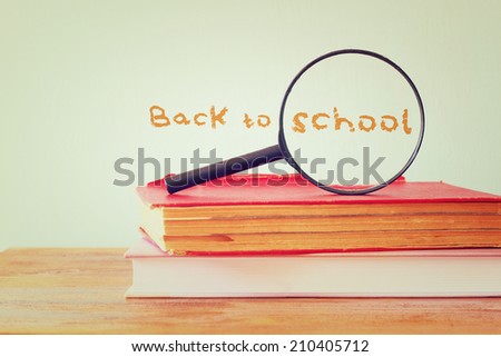 back to school background with stack of books and magnifying glass. filtered image.
