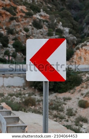 
Left turn sign: Road signs warn of a sharp turn on a narrow, rocky road. 
Traffic safety. Road barrier. Attention concept.