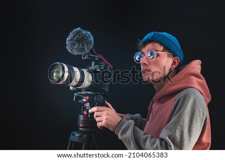 Filmmaker or cinematographer using professional camera gear to make documentaries and movies. Young cameraman, audiovisual, story telling and directing movies concepts. Royalty-Free Stock Photo #2104065383