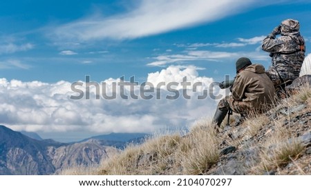 Hunters in the mountains are searching for cautious animals with binoculars and telescope. Hunters in the high mountains are searching for animals using optical devices.  Royalty-Free Stock Photo #2104070297