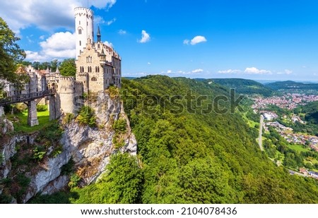 Lichtenstein Castle on mountain top in summer, Germany, Europe. This famous castle is landmark of Schwarzwald, Baden-Wurttemberg. Scenic view of fairytale Lichtenstein Castle and city in distance.  Royalty-Free Stock Photo #2104078436