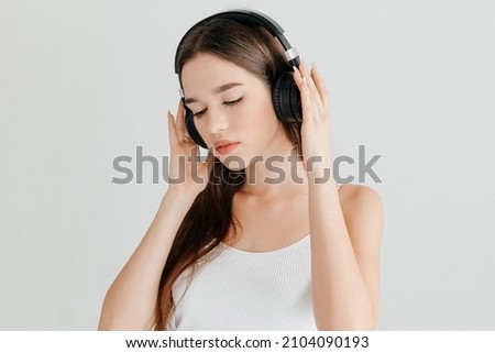 Young woman wearing casual clothes - white top and jeans, black headphones, listening to her favorite song