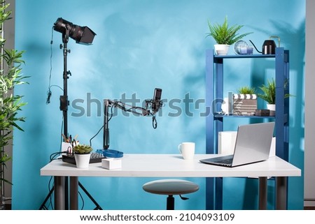 Empty online radio studio broadcasting room with professional microphone and video light used for podcast transmission. Video podcasting setup with digital mixer console and laptop computer. Royalty-Free Stock Photo #2104093109