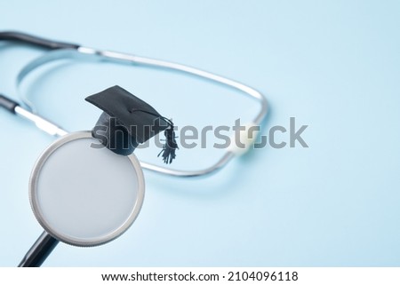 Graduation hat on doctor stethoscope mock up, blue background with copy space. Medical school, health care education or doctor's university degree concept