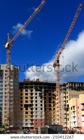 Two cranes are building a multi-storey residential building of brick in summer on  background of clouds and sky