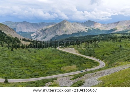 Cottonwood Pass - A panoramic Summer day view of a mountain road winding in a green valley at east of  the summit of Cottonwood Pass. Buena Vista - Crested Butte, Colorado, USA. Royalty-Free Stock Photo #2104165067