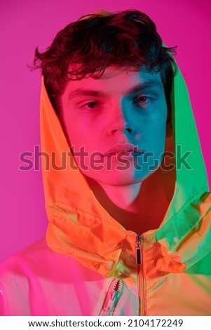 Fashionable youth style. Portrait of a cool guy posing in a bright yellow jacket with a hood on his head. Bright pink background. Creative designer clothes. Close up portrait. Royalty-Free Stock Photo #2104172249