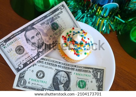 Birthday cupcake with gift money. White cake with white frosting and rainbow sprinkles. Colorful party hats. President's day concept. Funny fun concept.