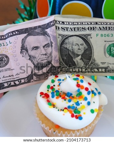 Birthday cupcake with gift money. White cake with white frosting and rainbow sprinkles. Colorful party hats. President's day concept. Portraits of the presidents. Funny fun concept.