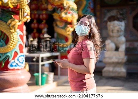 Portrait of asian woman traveler wear protective mask germs is looking up information on smartphone at Chinese buddhist temple or shrine,Prevention of the spread of COVID-19 virus,Chinese New Year