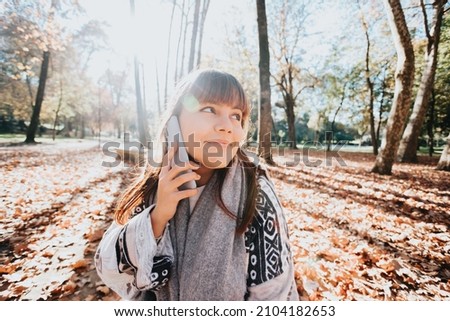 Young woman having a fun call during a sunset at the forest during an autumnal winter day. Connectivity and social concept.Young people life style. Greeting friends online. Copy space.