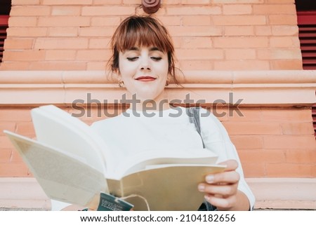 Young woman on white shirt holding and reading a book at the train station, reading everywhere people, book hobby fan. Waiting for the train to come, killing free time activities and habits Royalty-Free Stock Photo #2104182656