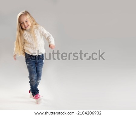Happy pretty beautiful little girl walking at studio white background, copy space, wearing white sweater with denim pants