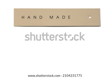 Clothes tag of rectangle shape positioned horizontally on white background, with small hole in right side with inscription on it indicating that product hand made. 