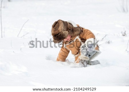 A child in a winter fur coat, hat and felt boots in a snowy forest.A boy in winter Russian folk clothes crawls through snowdrifts.Winter picture, like in a fairy tale