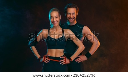Gym and fitness concept. Strong athletic woman and man on black background wearing in the sportswear. Royalty-Free Stock Photo #2104252736