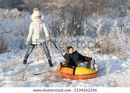 Elder sister and her little brother riding snow tube on sunny winter morning. Happy kids faces. Funny games on winter vacation. Everything is white, frosty trees around.
