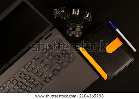 Photo of an old camera with a computer on a black background. And also a notebook with a pen. For designers or at your request.