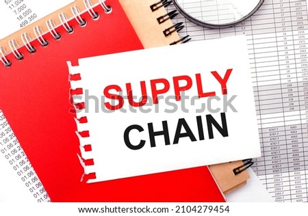 On a light background - reports, a magnifying glass, brown and red notepads, and a white notepad with the text SUPPLY CHAIN. Business concept