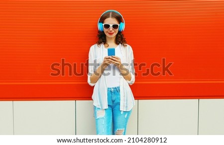 Portrait of smiling young woman in headphones listening to music with smartphone on red background