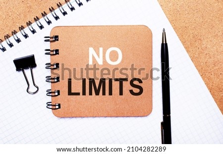 On a wooden background notepad, black pen, paper clip and brown notepad with the text NO LIMITS. Business concept