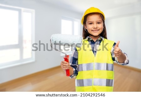 building, construction and profession concept - smiling little girl in protective helmet and safety vest with paint roller showing thumbs up over empty room on background