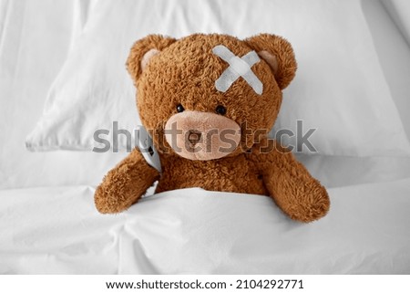medicine, healthcare and childhood concept - ill teddy bear toy with medical patch on head and thermometer lying in bed Royalty-Free Stock Photo #2104292771
