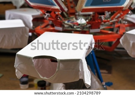 a white t-shirt on wooden shelve of the print screening apparatus. serigraphy production. printing images on t-shirts Royalty-Free Stock Photo #2104298789