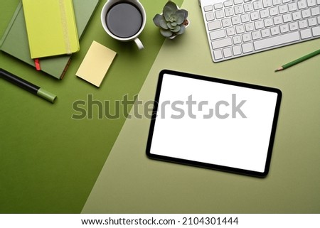 Top view digital tablet with empty screen and supplies on green background.