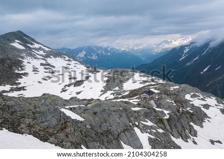 A mountain hut in the Ticino mountains in spring. Snow is around the hut and the surrounding mountains.